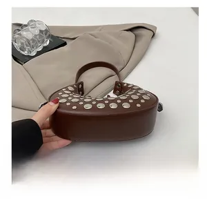 Close-up of brown crescent handbag with silver punk-style studs and polished PU texture