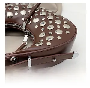 Detail of silver rivets and metal zipper on dark brown leather shoulder bag