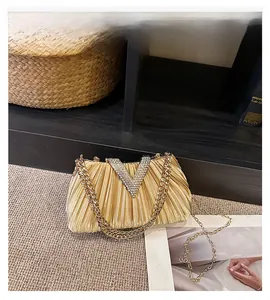 Détail d'une pochette dorée plissée avec boucle en strass en V et bandoulière chaîne