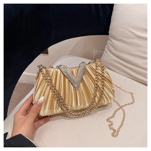 Détail d'une pochette plissée or champagne avec boucle en strass en V et chaînes dorées