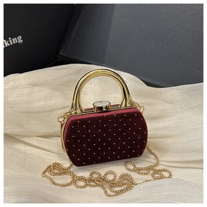 Détail de pochette en velours bordeaux clouté de cristaux avec poignée dorée sur tissu