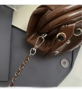 Dettaglio del gancio in metallo argento e tracolla in pelle intrecciata su borsa a pieghe