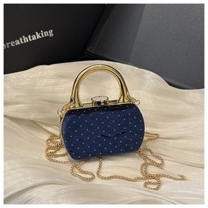 Détail d'une pochette en velours bleu avec clous dorés et poignée sur fond de soie