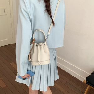 Chic beige bucket bag in lychee leather shown on a model in a minimal indoor setting