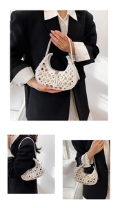 Detail view of white half-moon bag with silver rivets and sleek zipper closure