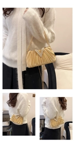 Détail de la pochette de soirée plissée dorée avec boucle V en strass et chaîne en métal
