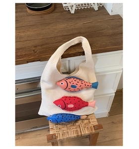 Détail du sac fourre-tout en tricot blanc cassé avec trois breloques de poissons colorés