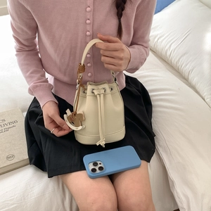 Chic beige bucket bag with drawstring closure and horse pendant in a lifestyle setting
