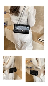 Detail of glossy black crocodile pattern shoulder bag with silver chain and square lock