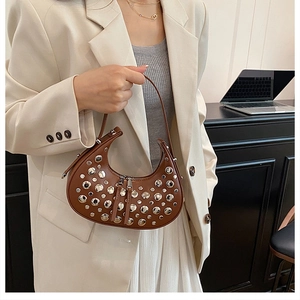 Detail of a brown leather crescent moon bag with silver rivets and sleek top handle