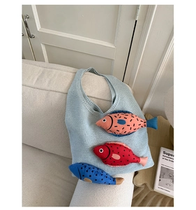 Détail d'un sac à main en tricot bleu clair orné de trois poissons 3D colorés sur sofa