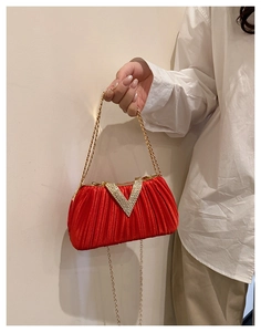 Détail d'une pochette rouge plissée avec boucle en strass en V et chaîne dorée