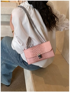 Detail of pink faux crocodile leather texture and silver chain strap on women's crossbody bag