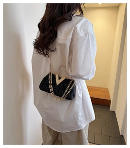Détail de la pochette de soirée plissée noire avec boucle en V en strass et chaîne dorée