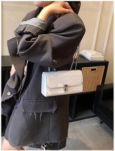 Detail view of a white crocodile pattern crossbody bag with silver chain strap on a model
