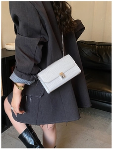 Detail of white crocodile texture crossbody bag with silver chain on model shoulder