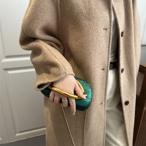 Elegant emerald green silk clutch bag with gold handle styled with a luxury camel coat