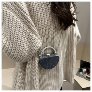 Détail du mini sac demi-lune scintillant avec poignée en métal sur un pull beige