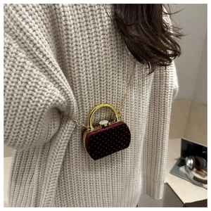 Détail du mini sac en velours bordeaux avec rivets dorés et chaîne sur un pull en maille