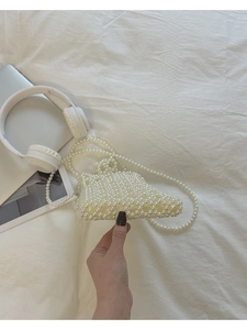 Détail d'un sac à bandoulière en perles blanches fait main posé sur un lit
