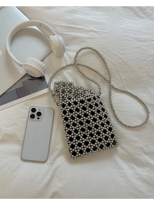 Détail du sac à bandoulière perlé argenté ajouré sur lin blanc avec divers accessoires