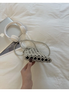 Vue détaillée du sac bandoulière en perles argentées tressées posé sur un lit blanc chic