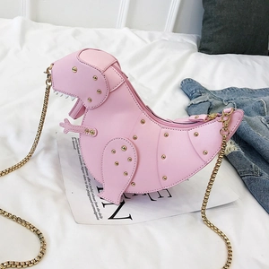 Rosafarbene Dinosaurier-Tasche mit Goldnieten und Metallkette auf weißem Bett