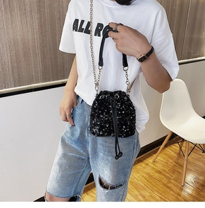 Detail view of black sequined bucket bag with metal chain strap on casual model