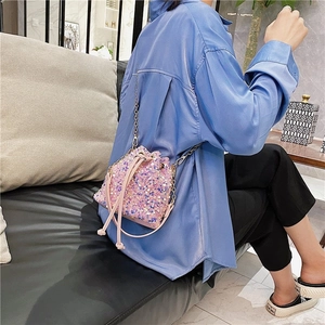 Pink sequin drawstring bucket bag with gold chain strap worn as a stylish crossbody bag