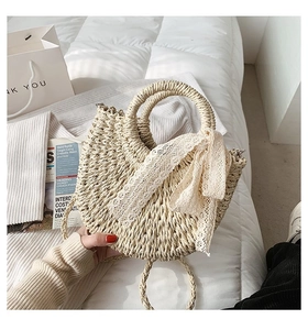 Detail of hand-woven straw beach bag featuring elegant white lace bow and round handles