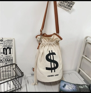 Detail of canvas drawstring bucket bag with dollar sign print and adjustable leather strap