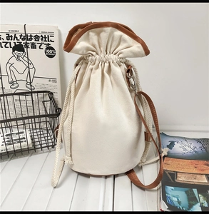 Detail of canvas drawstring bucket bag featuring brown leather trim and cotton rope closure