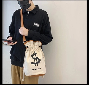 Detail of canvas drawstring bucket bag with leather base and shoulder strap in street style