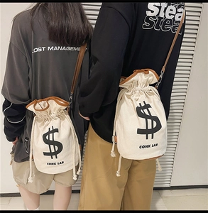 Detail view of the beige canvas drawstring bucket bag featuring black logo and leather strap