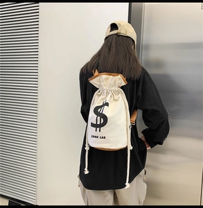 Detail of canvas drawstring backpack with dollar sign print and brown leather trim
