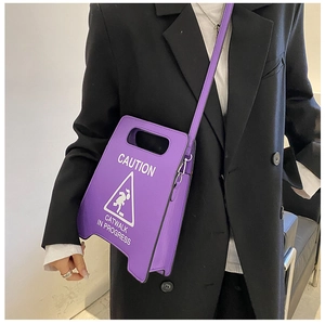Détail d'un sac bandoulière violet en forme de panneau porté sur un blazer noir chic