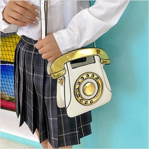 Détail d'un sac bandoulière blanc et doré en forme de téléphone porté par un mannequin