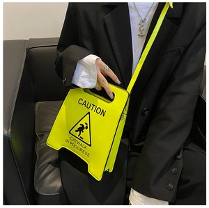 Détail du sac à bandoulière jaune fluo en forme de panneau de signalisation sur fond noir