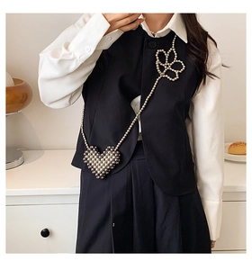 Detail of woven pearl strap crossbody bag with heart and flower charms on model