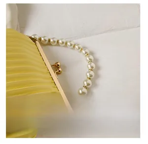 Close-up of yellow pleated shell bag featuring a large pearl handle and metal clasp