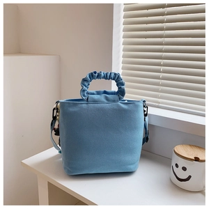 Close-up of a light blue pleated canvas tote bag with a cute plush doll charm detail