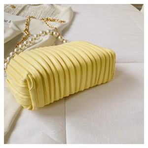 Detail of light yellow ruched shell bag featuring elegant pearl and gold chain handles