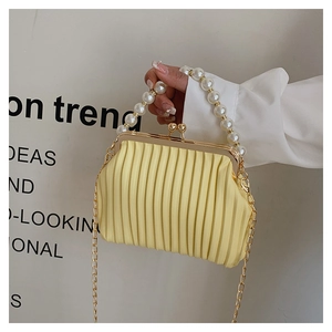 Detail of yellow pleated handbag featuring large pearl handle and gold chain strap