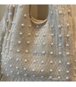 Detailed view of beige knit tote bag with pearl embellishments and fringe accents