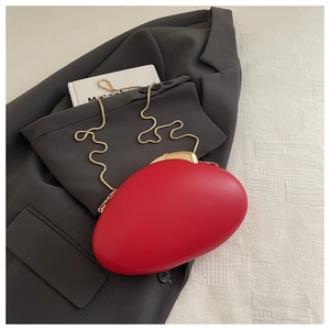 Macro detail of red oval acrylic clutch bag with gold snake chain on grey blazer