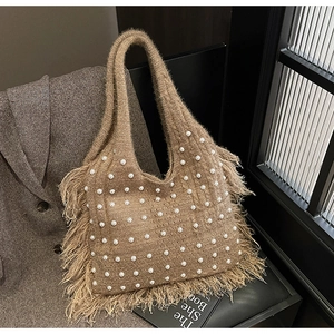 Detail of camel knit tote bag featuring white pearl accents and fringe edges on a chair
