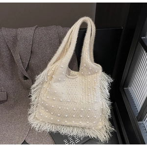 Detail of beige knitted tote bag featuring pearl embellishments and long fringe tassels