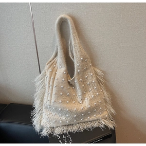Close-up of cream knit tote bag featuring white pearl accents and long side tassels