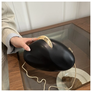 Detail of matte black pebble clutch bag with gold metal clasp and snake chain strap