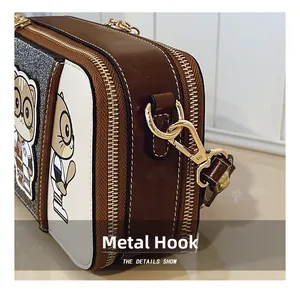 Detail of golden metal hooks and squirrel graphics on a brown cross-body camera bag